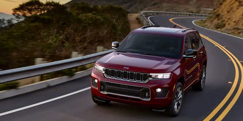 Image of the 2024 Jeep Grand Cherokee 4xe driving down a two-lane highway through a mountainscape