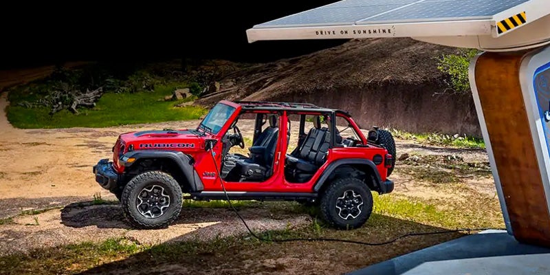 Image of the red 2024 Jeep Wrangler 4xe Rubicon edition parked and charging next to a charging station out in the wilderness