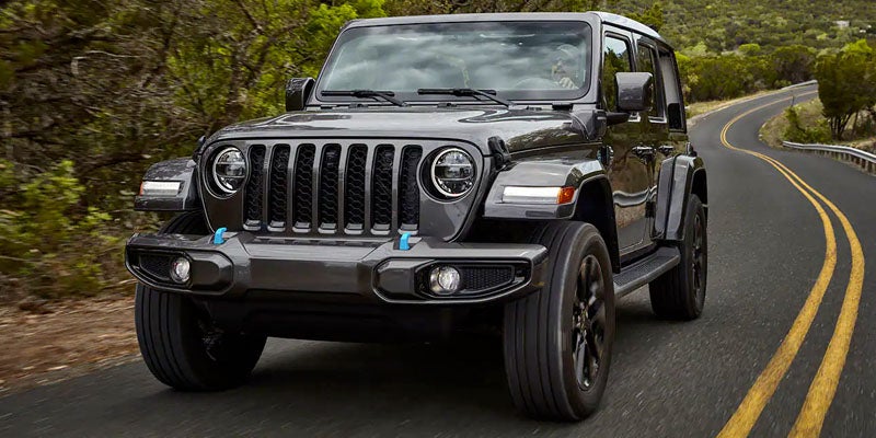 Image of the 2024 Jeep Wrangler 4xe driving down a single-lane highway through a natural wooded landscape