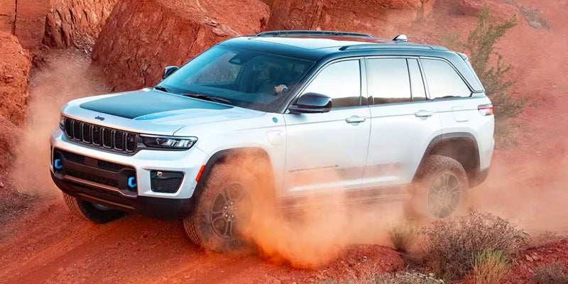 Image of a white 2024 Jeep Grand Cherokee off-roading over a desert landscape kicking up dust around the wheels