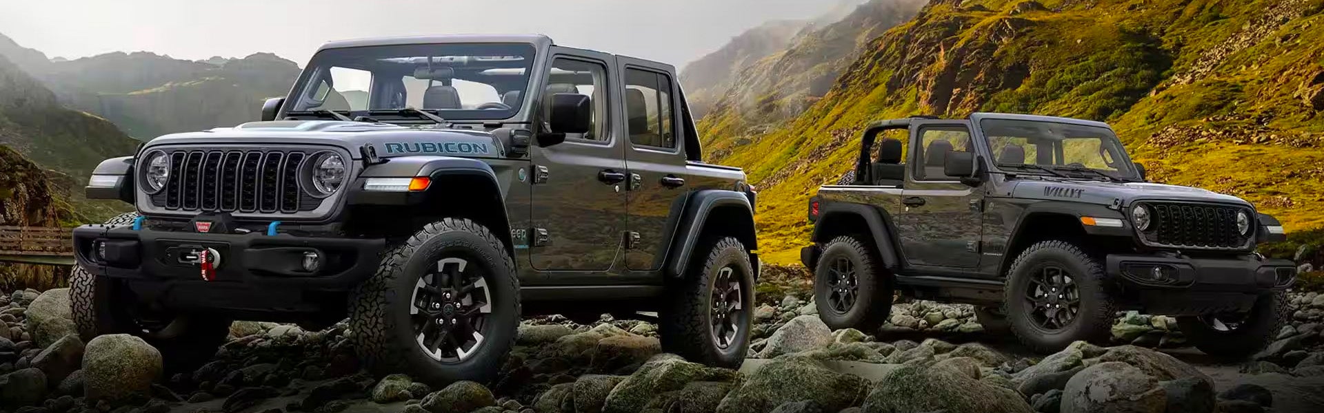 Hero image of two charcoal gray 2024 Jeep Wranglers taken at opposing front angles, featured in front of a mountainscape