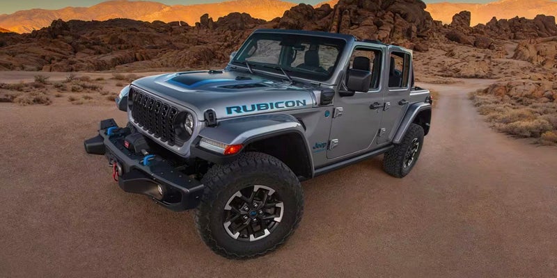 Image of a gray 2024 Jeep Wrangler taken with a wide-angle camera on a dirt road in a desert landscape
