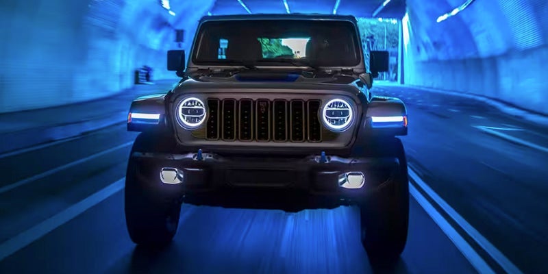 Image of a 2024 Jeep Wrangler driving through a tunnel toward the camera, with the tunnel lights reflecting blue on the subject and backdrop, blurring to indicate speed