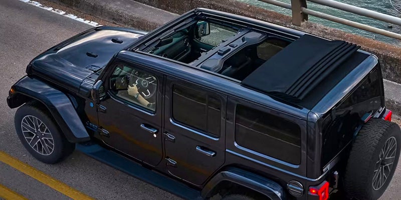Image of a black 2024 Jeep Wrangler driving away from the camera down a road, shot from a higher angle