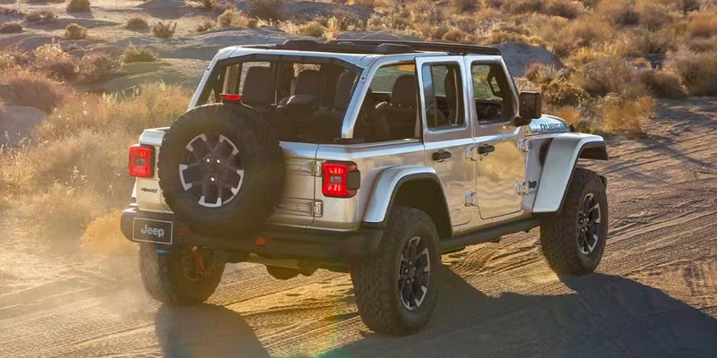 Image of a silver 2024 Jeep Wrangler that is driving away from the camera through a desert landscape