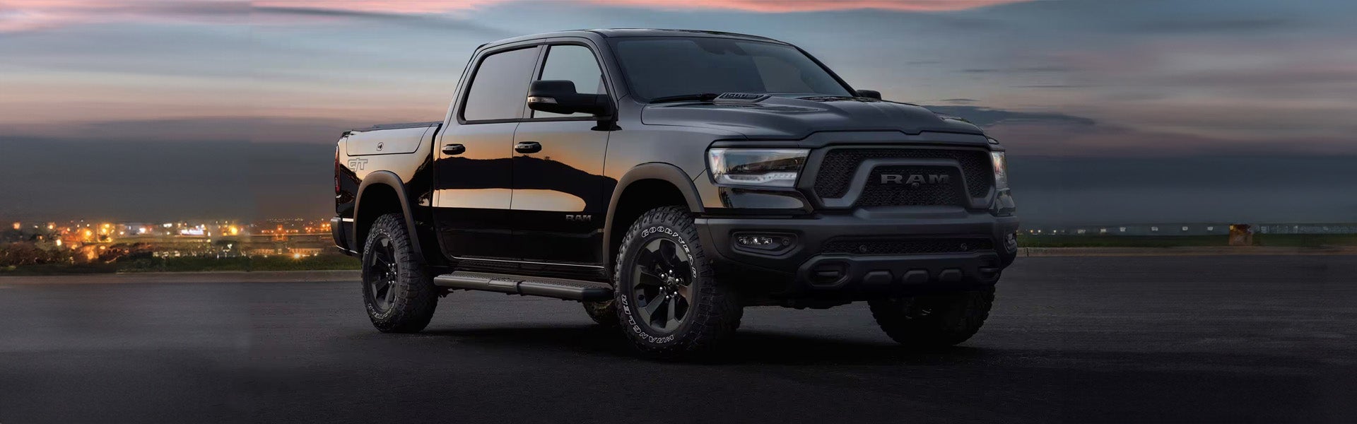 Hero image of a 2024 RAM 1500 parked in a paved parking lot in front of a lit cityscape backdrop
