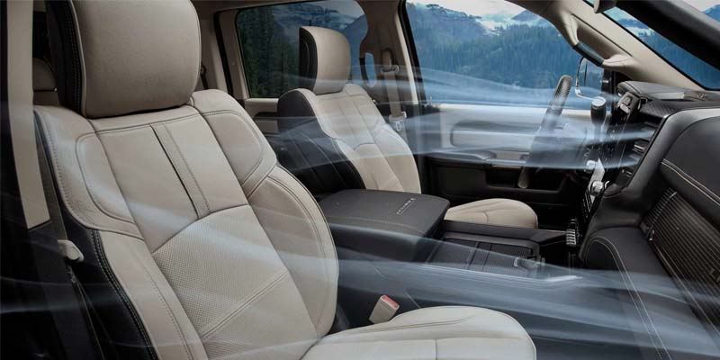 Interior image of the 2024 RAM 3500 featuring the front and passenger seats with light warm gray upholstery, showcasing the A/C capacity with photoshopped air currents