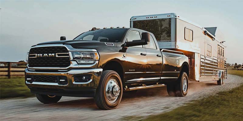 Image of the 2024 RAM 3500 towing a large horse/cattle trailer down a gravel road through pasture