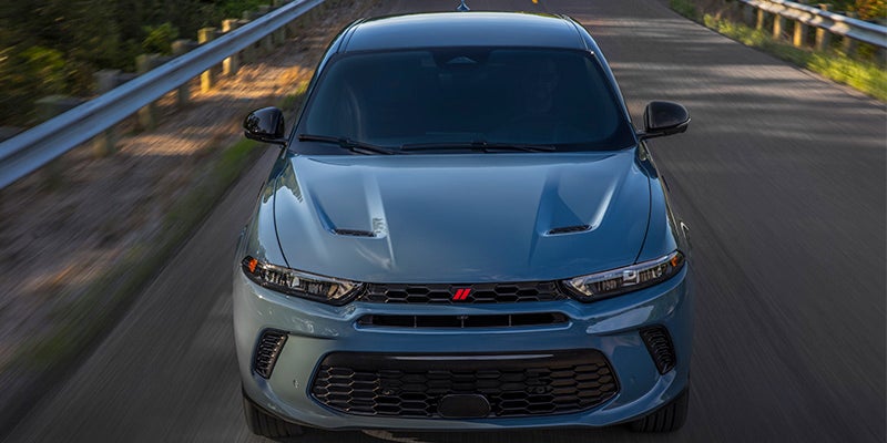 Image of the 2024 Dodge Hornet driving toward the camera shot at a higher angle, featuring a paved road and guardrails that are blurred to indicate that the vehicle is in motion