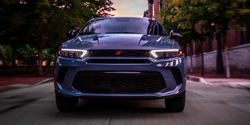 Image of the 2024 Dodge Hornet driving head-on toward the camera through a street lined with planted trees in a city