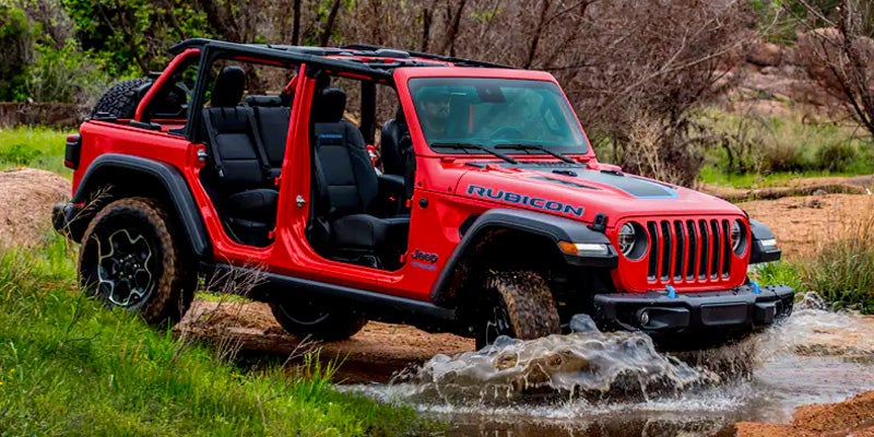 Image of the red 2024 Jeep Wrangler 4xe Rubicon Edition driving through a mud puddle on a dirt path through a ntural landscape