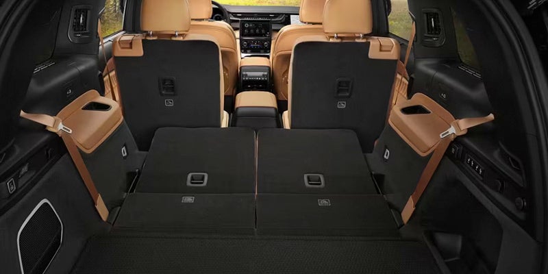 Image of the interior of a 2024 Jeep Grand Cherokee, featuring tan leather seating, with the middle row folded down to showcase the roomy storage space