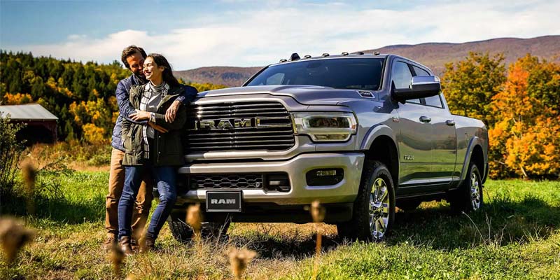 Image of the 2024 RAM 2500 parked in a grassy knoll with mountains in the backdrop, showing a man and a woman smiling and hugging each other while leaning against the truck