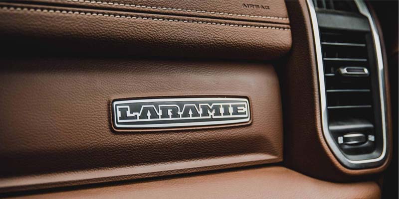 Close-up image of the 2024 RAM 3500 Laramie emblem on the front dashboard next to an air vent, displayed on brown leather interior