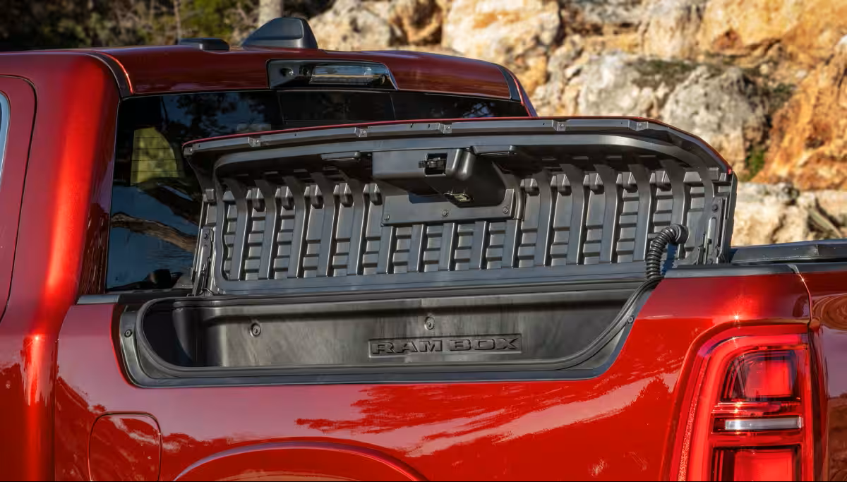 Image of a red 2024 RAM 1500 driving toward the camera on a highway in the desert, towing a white and chrome trailer